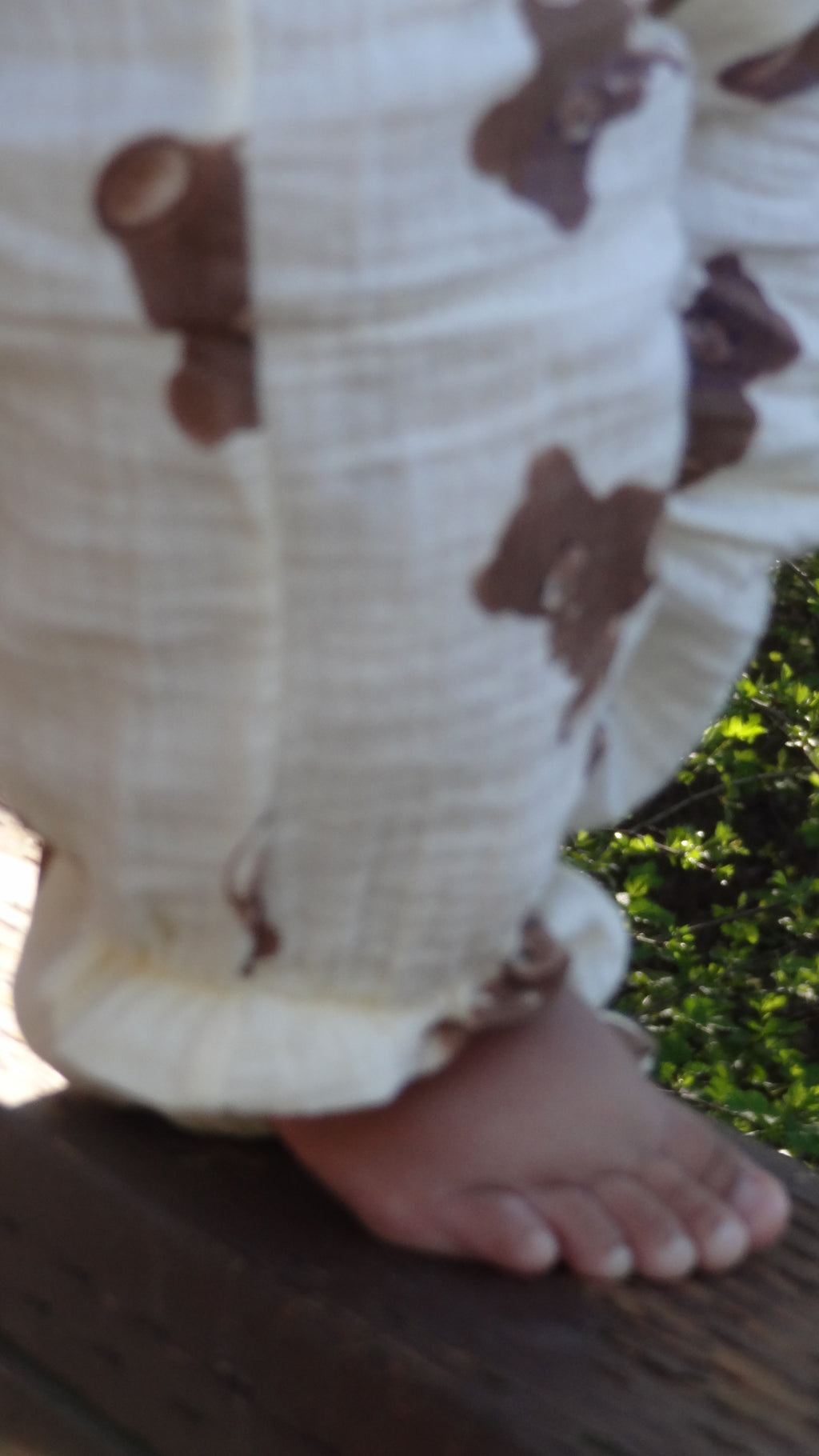 Close-up of a person's foot wearing a white sock with brown bear patterns, standing on a wooden surface with greenery in the background.