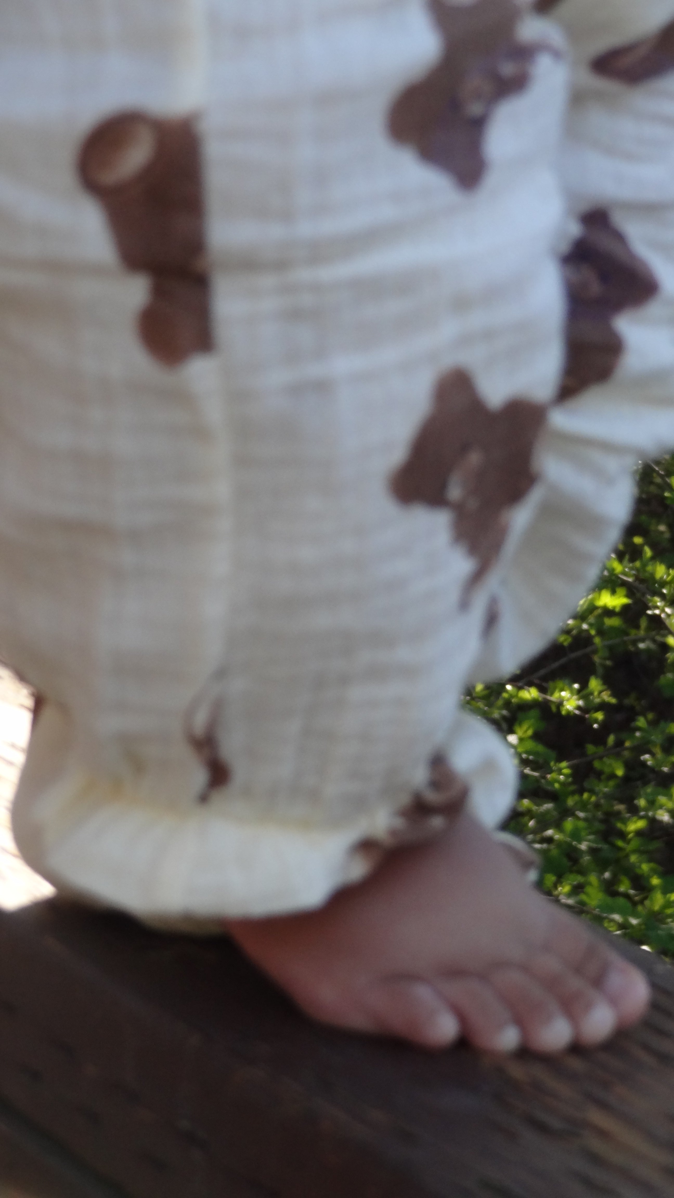 Close-up of a person's foot wearing a white sock with brown bear patterns, standing on a wooden surface with greenery in the background.