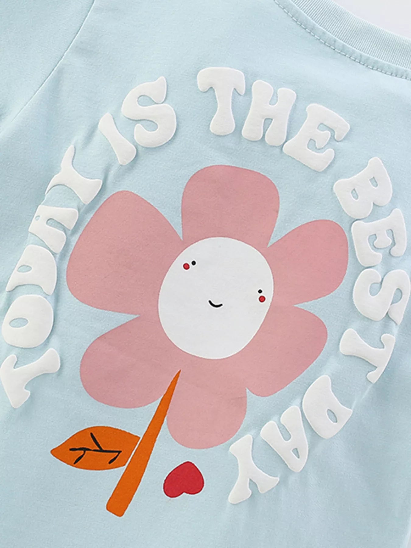 Light blue shirt with a pink flower and text on a light blue background