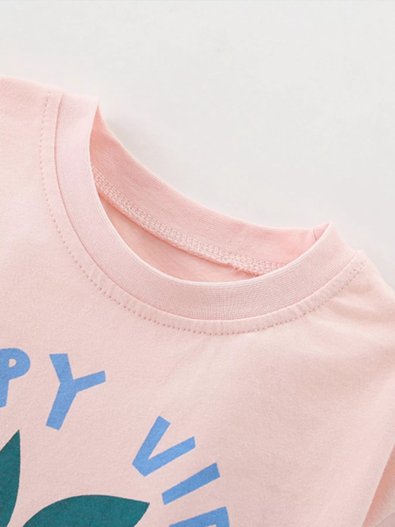 Close-up of a pink shirt with blue and green text on a light gray background
