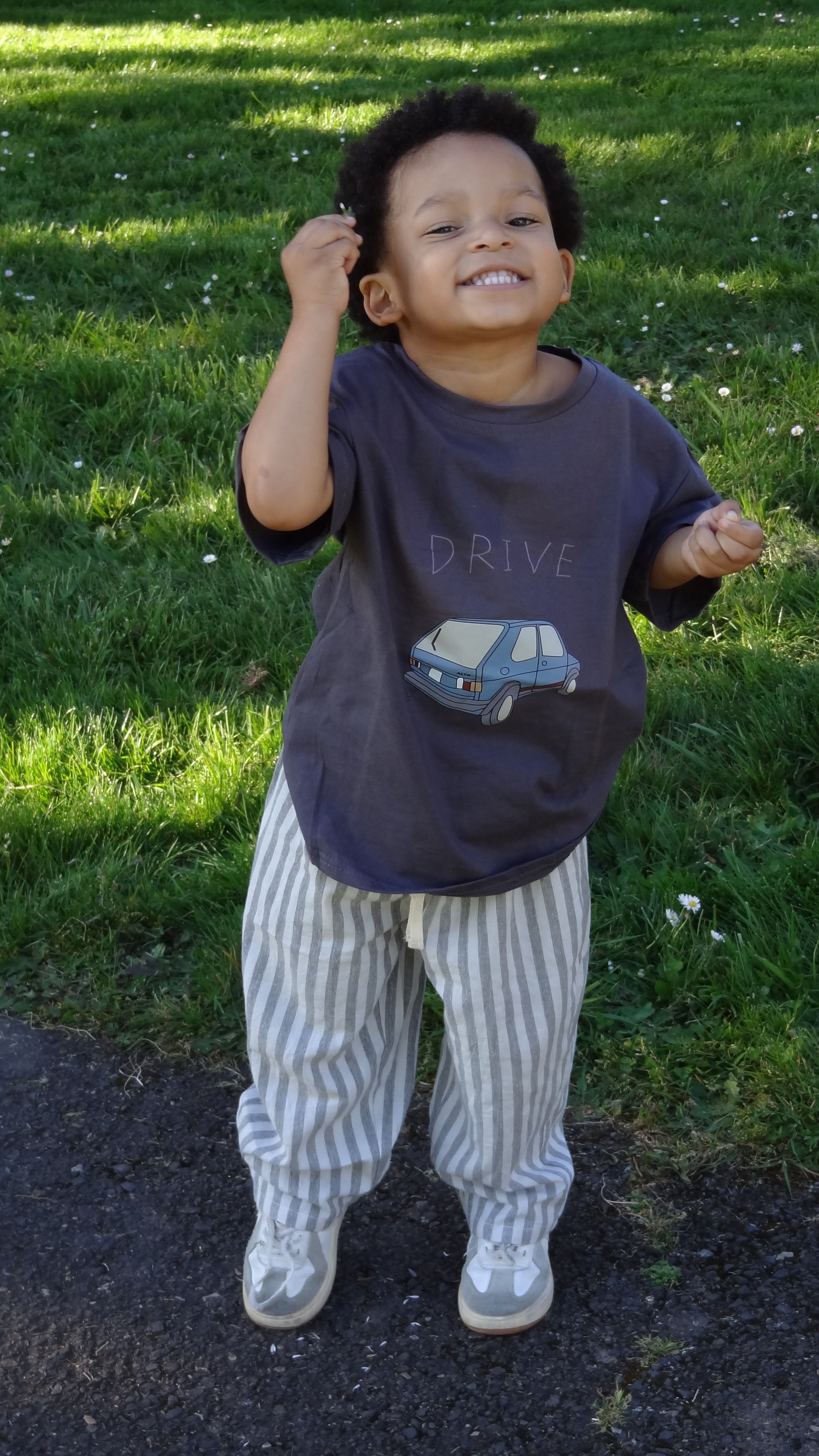 child standing on a grassy area with one wearing a striped outfit and the other in a dark shirt.