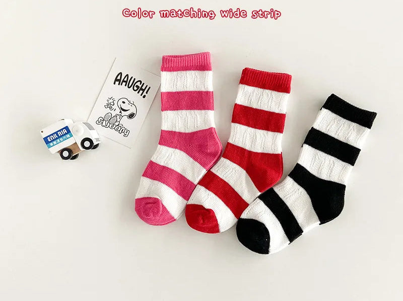 Three pairs of striped socks in pink, red, and black on a white background with a small package labeled 'AAUGH!' in the corner.