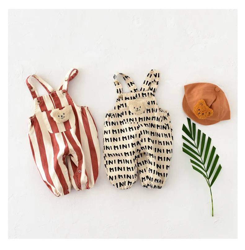 Two children's outfits with a striped romper and patterned overall, accompanied by a brown hat and green leaf on a white background.