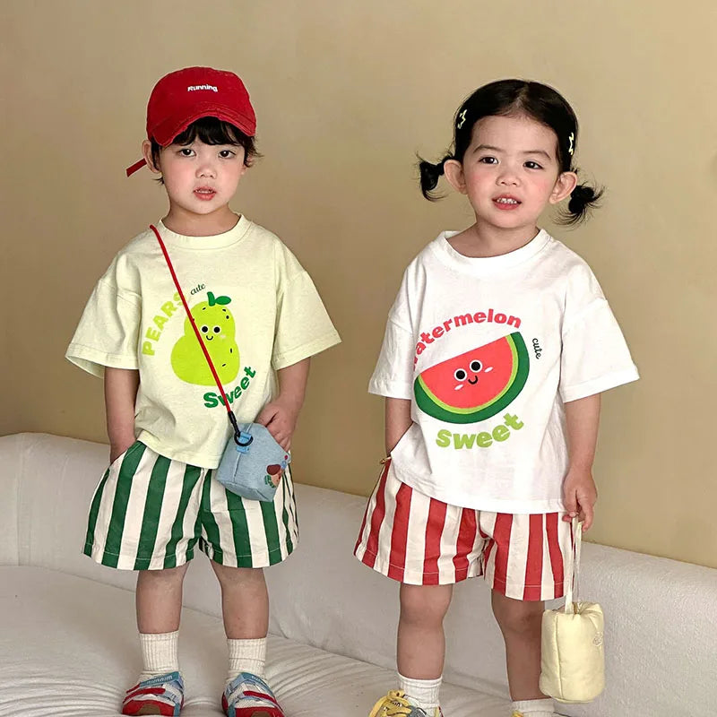 Two children wearing matching outfits with fruit-themed designs on a beige background.