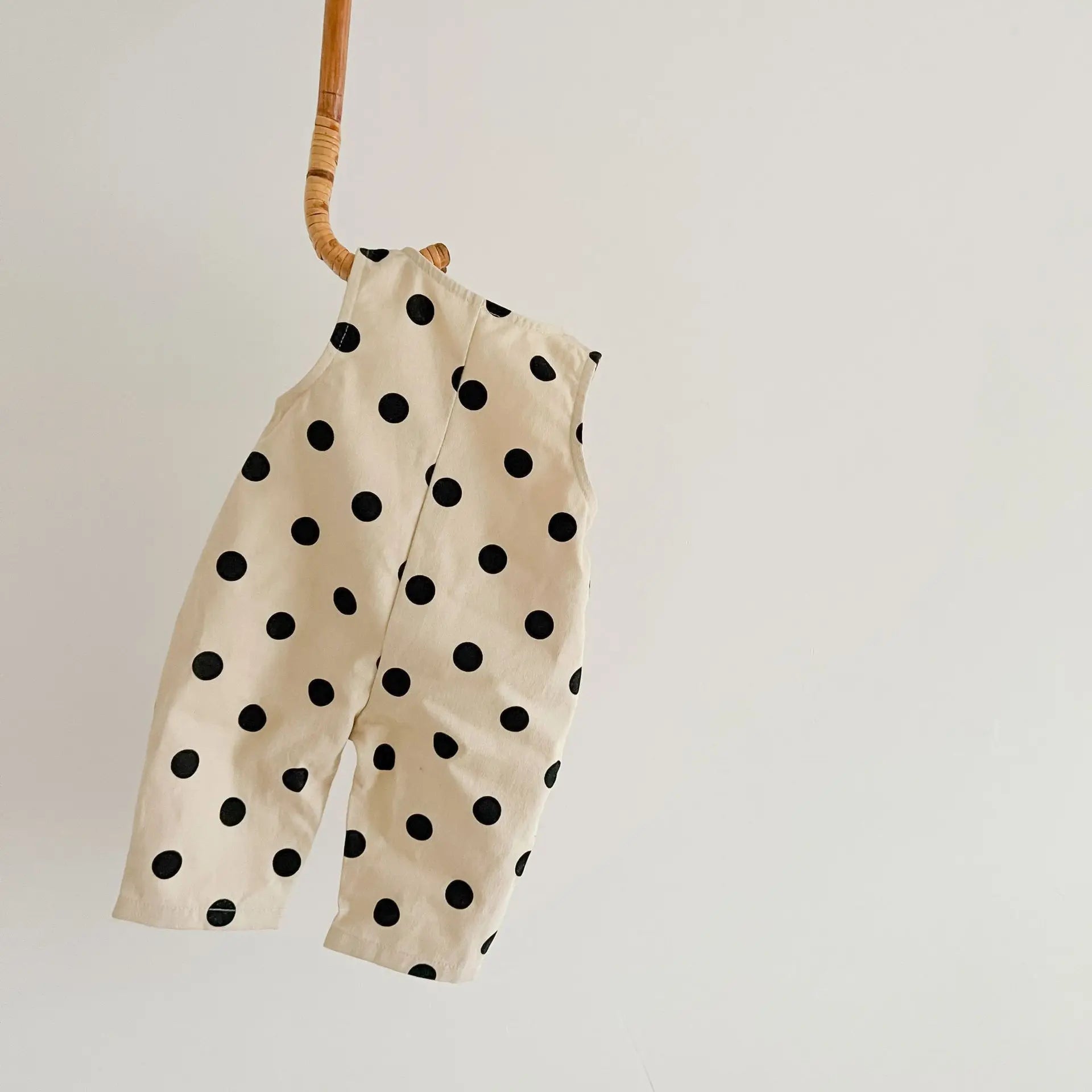 Beige romper with black polka dots hanging on a wooden rod against a light background