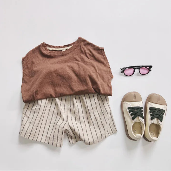 Children's outfit with brown top, striped shorts, sneakers, and sunglasses on a light gray background.