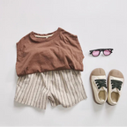 Children's outfit with brown top, striped shorts, sneakers, and sunglasses on a light gray background.