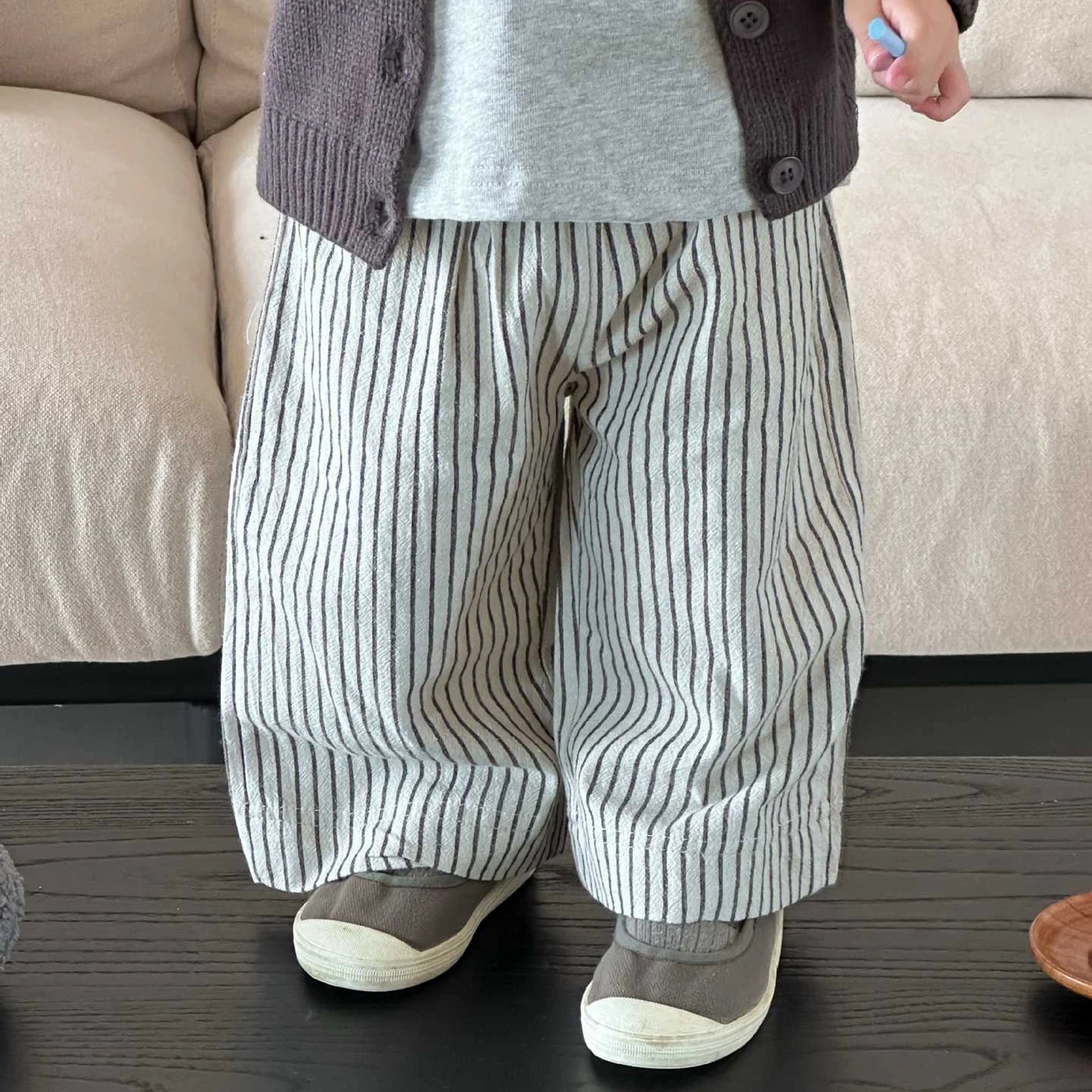 Person wearing striped pants and a gray sweater in front of a beige couch.
